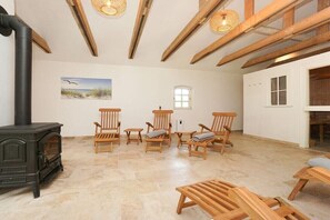 A spacious room with a wood-burning stove, several wooden chairs, a table, and a painting of a beach scene on the wall.