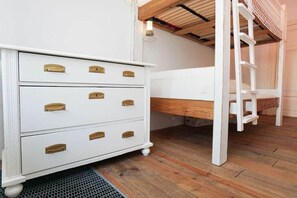 A white dresser with brass handles, a wooden bunk bed with a ladder, and a wooden floor.