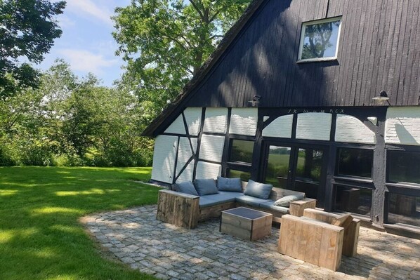 A large barn-style building with a stone patio, wooden furniture, and a view of the surrounding greenery.