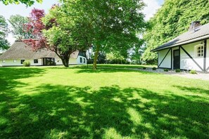 Ein traditionelles Haus mit einem Reetdach, umgeben von einem gepflegten Rasen und Bäumen.