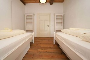 Ein Schlafzimmer mit zwei Betten, Holzboden, weißen Wänden und einer Tür.