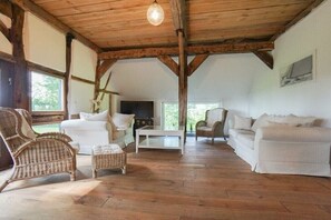 A rustic interior with exposed wooden beams, white furniture, and a fireplace.