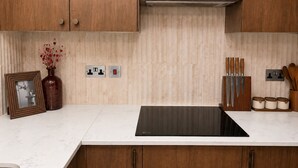 A kitchen with wooden cabinets, a black induction cooktop, and a tiled backsplash. - Modern Gated Retreat | Secure Parking & Patio | Great transport links (Croydon)