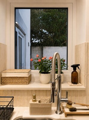 Ein modernes Badezimmer mit integriertem Waschbecken, einem Fenster mit Blick auf Grünflächen, einer Topfpflanze und einer Sprühflasche.