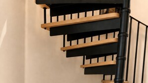 A staircase with black railings and wooden steps, a striped ottoman, and a woven rug on the floor. - Modern Gated Retreat | Secure Parking & Patio | Great transport links (Croydon)