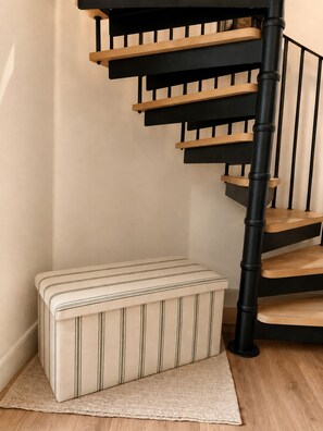 Eine Treppe mit schwarzen Geländern und Holzstufen, ein gestreifter Hocker und ein gewebter Teppich auf dem Boden.