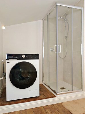 A compact room with a washing machine and a glass-enclosed shower. - The Sun's Attic (Sestu)