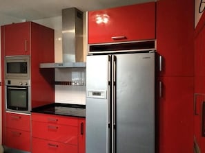 Een keuken met rode kasten, een roestvrijstalen koelkast en een magnetron.