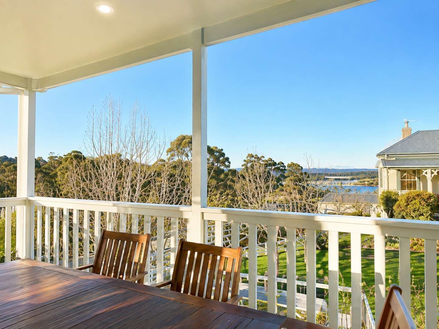 A covered outdoor area with a table and chairs, overlooking a scenic landscape with trees and a distant view of a house.