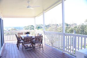 A covered outdoor area with a table and chairs, a ceiling fan, and a view of trees and hills.