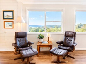 A room with two leather chairs, a wooden table, a lamp, and framed pictures on the wall. - Star of the Sea Milton Mollymook (Milton)