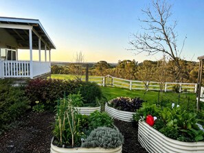 A garden with raised beds, a white fence, and a building with a porch. - Star of the Sea Milton Mollymook (Milton)