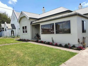 A residential house with a front porch, a small garden with flowers, and a clear sky.