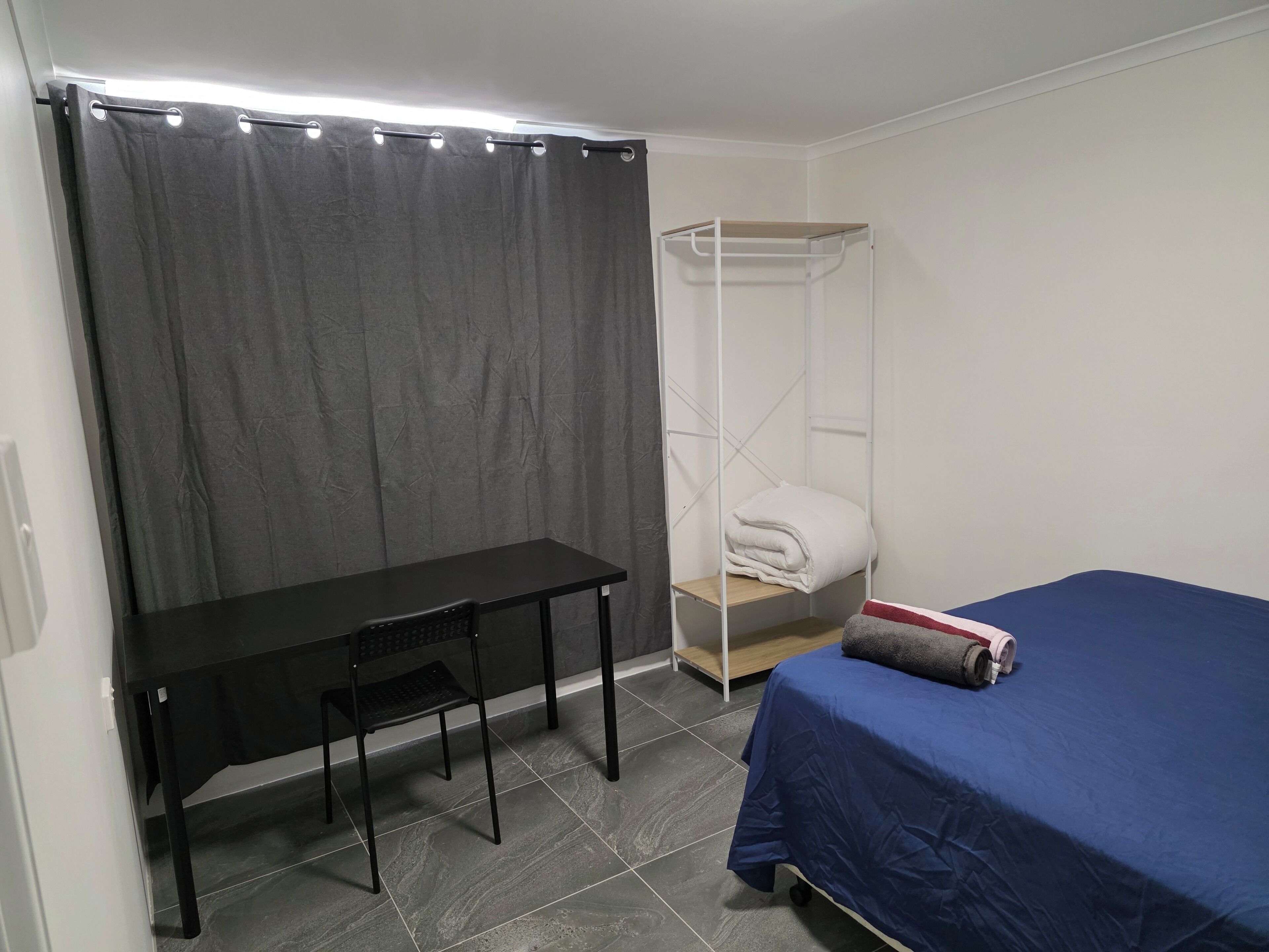 A room with a bed, a desk, a chair, a wardrobe, and a curtain.
