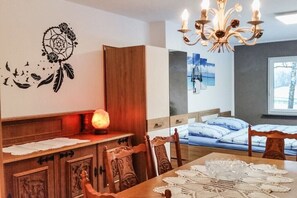 A dining area with a wooden table, chairs, a chandelier, a wall art piece, and a bed with a view. - Holiday apartment with 3 bedrooms (Sinspelt)