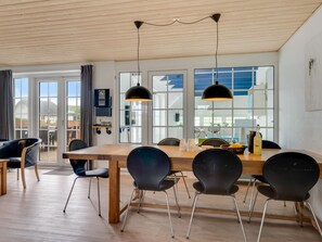Ein Essbereich mit Holztisch, schwarzen Stühlen, Pendelleuchten und großen Fenstern mit Blick nach draußen.