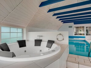 Ein moderner, überdachter Pool mit Whirlpool, weißen Wänden und blauen Deckenbalken.
