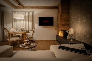 A cozy living room with a fireplace, a dining area with a table set for two, and a flat-screen TV mounted on the wall.