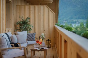 En træterrasse med en sofa, et bord med drikkevarer og et magasin, og udsigt til grønne omgivelser.