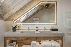 A bathroom with a wooden ceiling, a large mirror, two sinks, and a towel rack. - Chalet Apartment with Sauna for 2 Guests | at Lake Wolfgang | schwalbenNEST (Strobl)