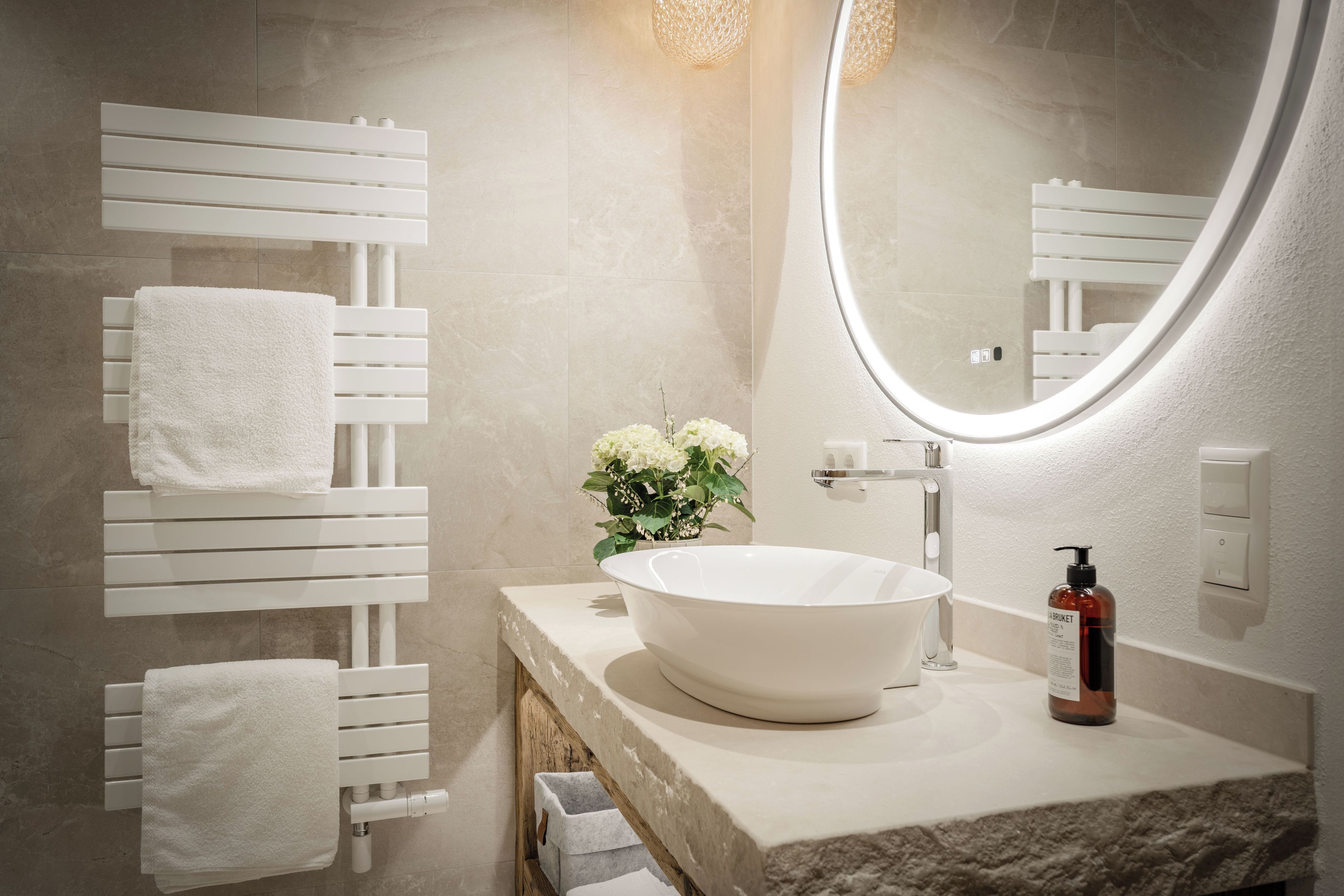 Un baño con un lavabo blanco, un espejo redondo y un perchero para toallas.