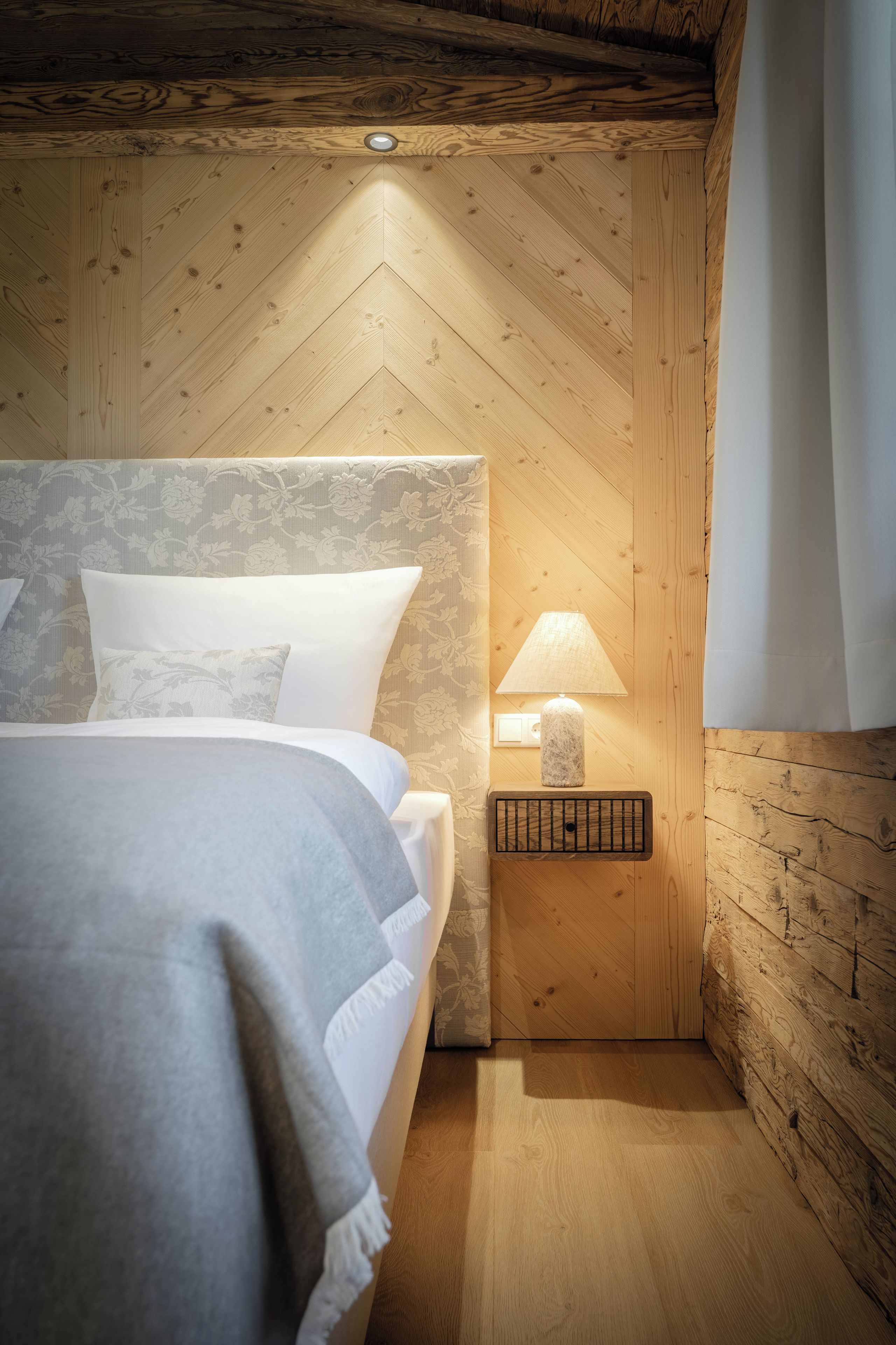 Habitación con paneles de madera, una cama, una mesita de noche con lámpara y una ventana con cortinas.