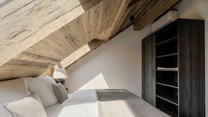 A bedroom with a sloped ceiling, a bed with pillows, a bedside lamp, and a wardrobe. - Luxury Apartment at Lake Wolfgang | with Hot Tub for 4 Guests | panoramaNEST (Strobl)