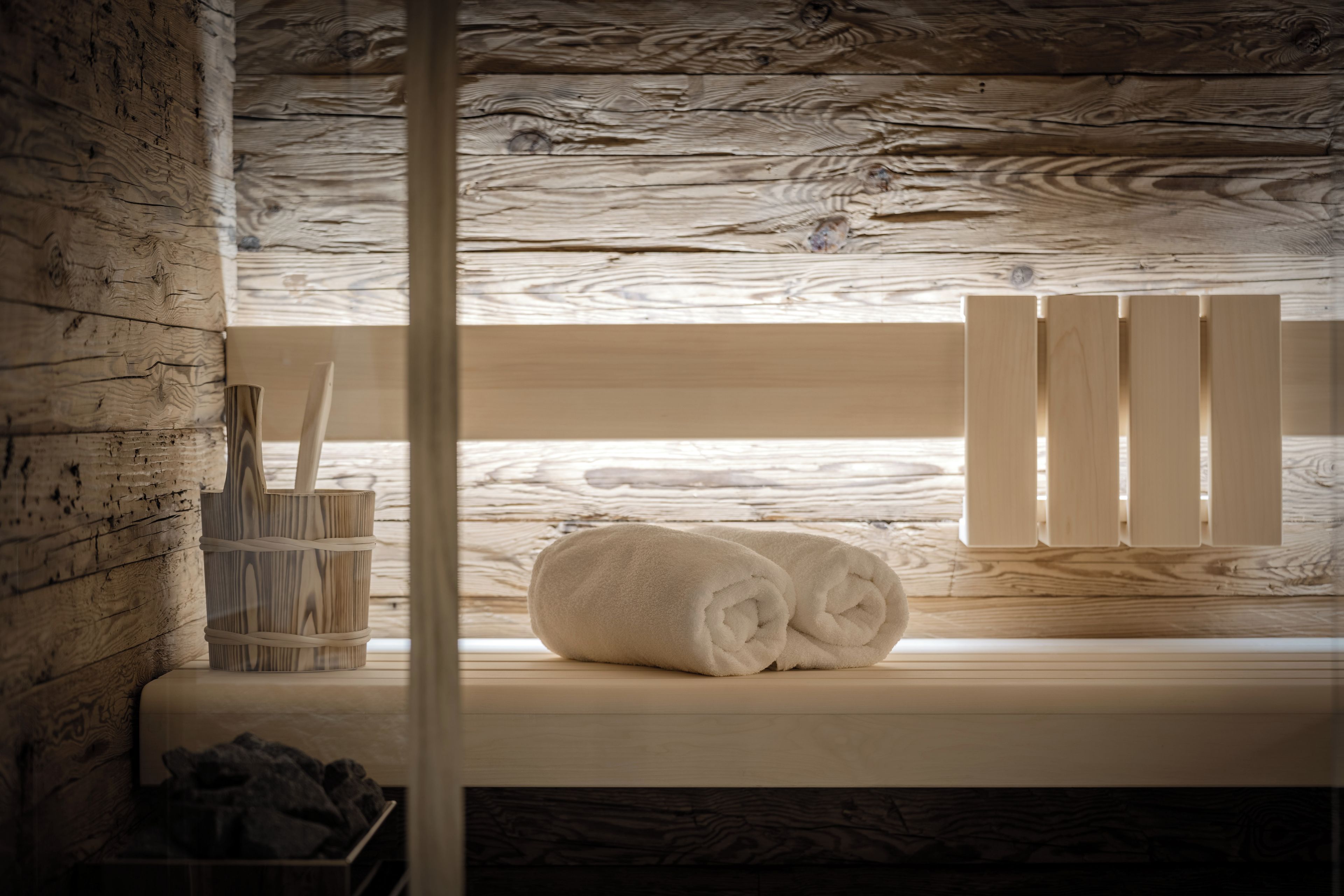 A wooden cabin interior with a window, a wooden bench, and a pair of rolled towels.