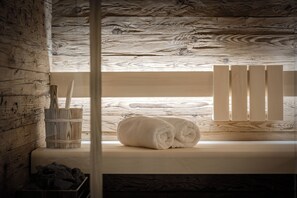 A wooden cabin interior with a window, a wooden bench, and a pair of rolled towels.