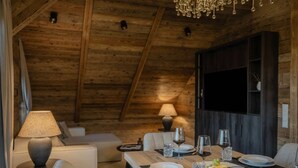 A cozy dining area with a wooden table set for two, a sofa, and a lamp. - Luxury Apartment at Lake Wolfgang | with Hot Tub for 4 Guests | panoramaNEST (Strobl)