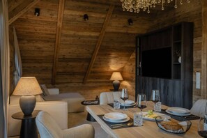 A cozy dining area with a wooden table set for two, a sofa, and a lamp. - Luxury Apartment at Lake Wolfgang | with Hot Tub for 4 Guests | panoramaNEST (Strobl)