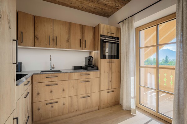 A kitchen with wooden cabinets, a stainless steel oven, a sink, and a window with a view of greenery and mountains.