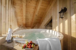 A wooden cabin with a hot tub, a bottle of champagne, a glass of wine, and a plate of strawberries. - Luxury Apartment at Lake Wolfgang | with Hot Tub for 4 Guests | panoramaNEST (Strobl)