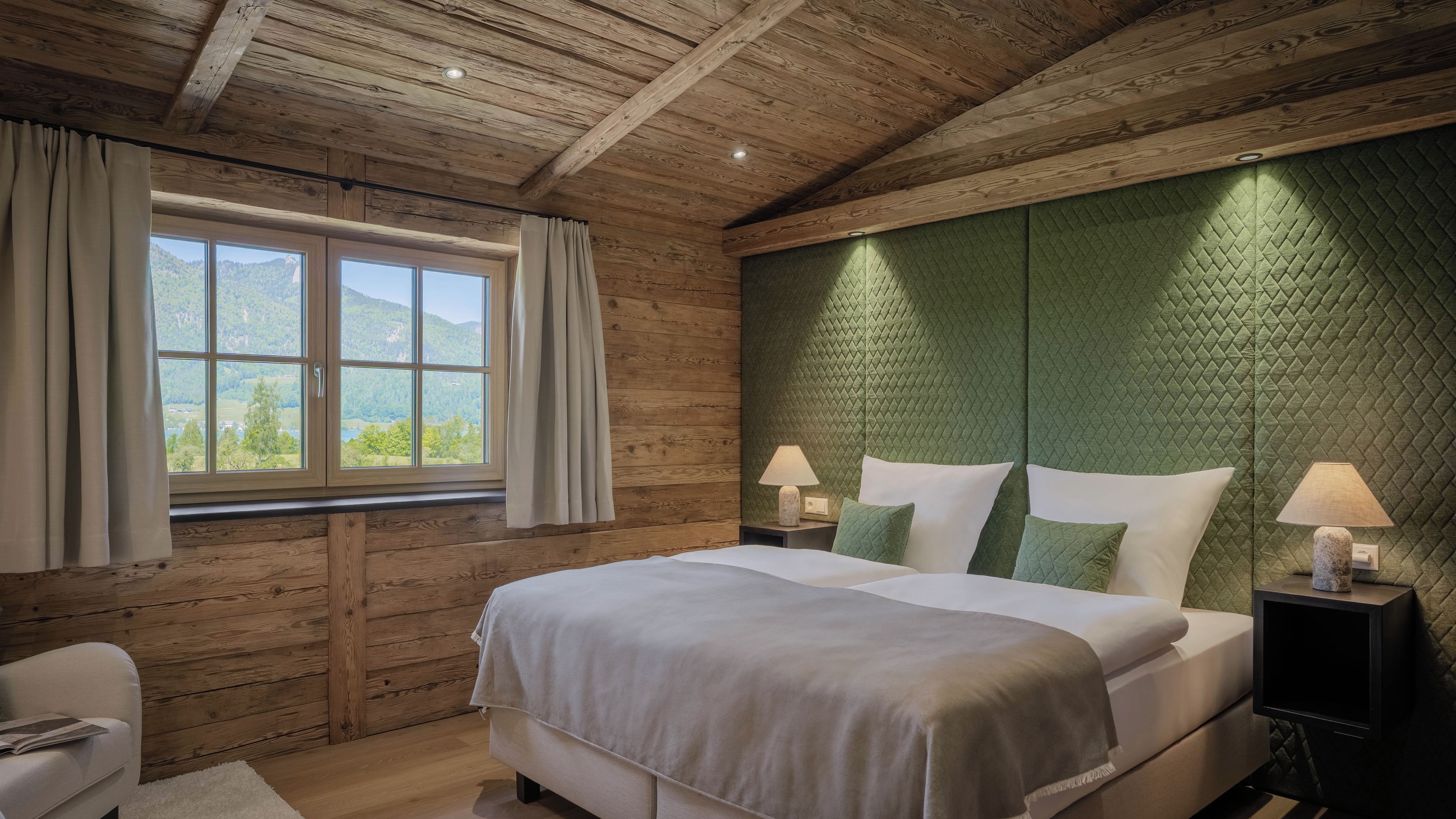 Un dormitorio con techo de madera, una cama grande, dos mesitas de noche con lámparas y vistas al exterior a través de una ventana.