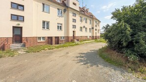 A multi-story building with a brick base and beige upper floors, a gravel driveway, and a large tree to the right. - Lilac Studio with Bathtub | Close to the Park (Wrocław)