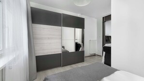 A modern bedroom with a bed, a large wardrobe, and a radiator. - Lilac Studio with Bathtub | Close to the Park (Wrocław)