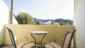 En balkong med ett litet runt bord och två stolar, med utsikt över ett bostadsområde och kullar i bakgrunden.