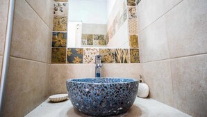 Ett badrum med ett handfat i mosaik, en spegel och mönstrade kakelplattor.
