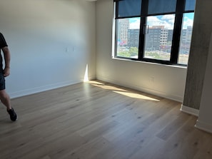 Een kamer met houten vloeren, een groot raam en uitzicht op gebouwen.