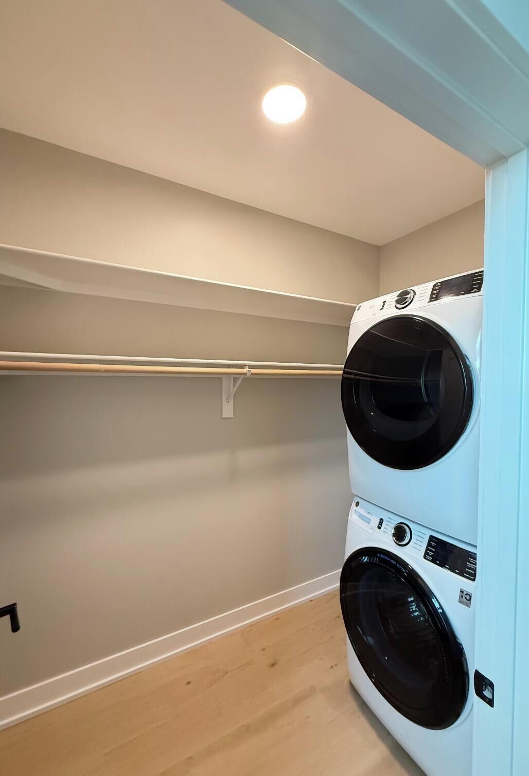 Une buanderie équipée de deux machines à laver à chargement frontal superposées, avec un plancher en bois et un mur de couleur claire.