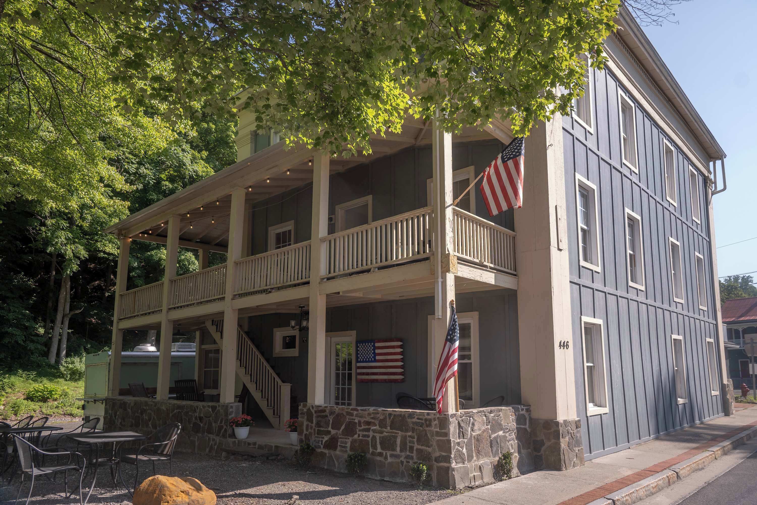A two-story building with a porch, stone foundation, and an American flag.