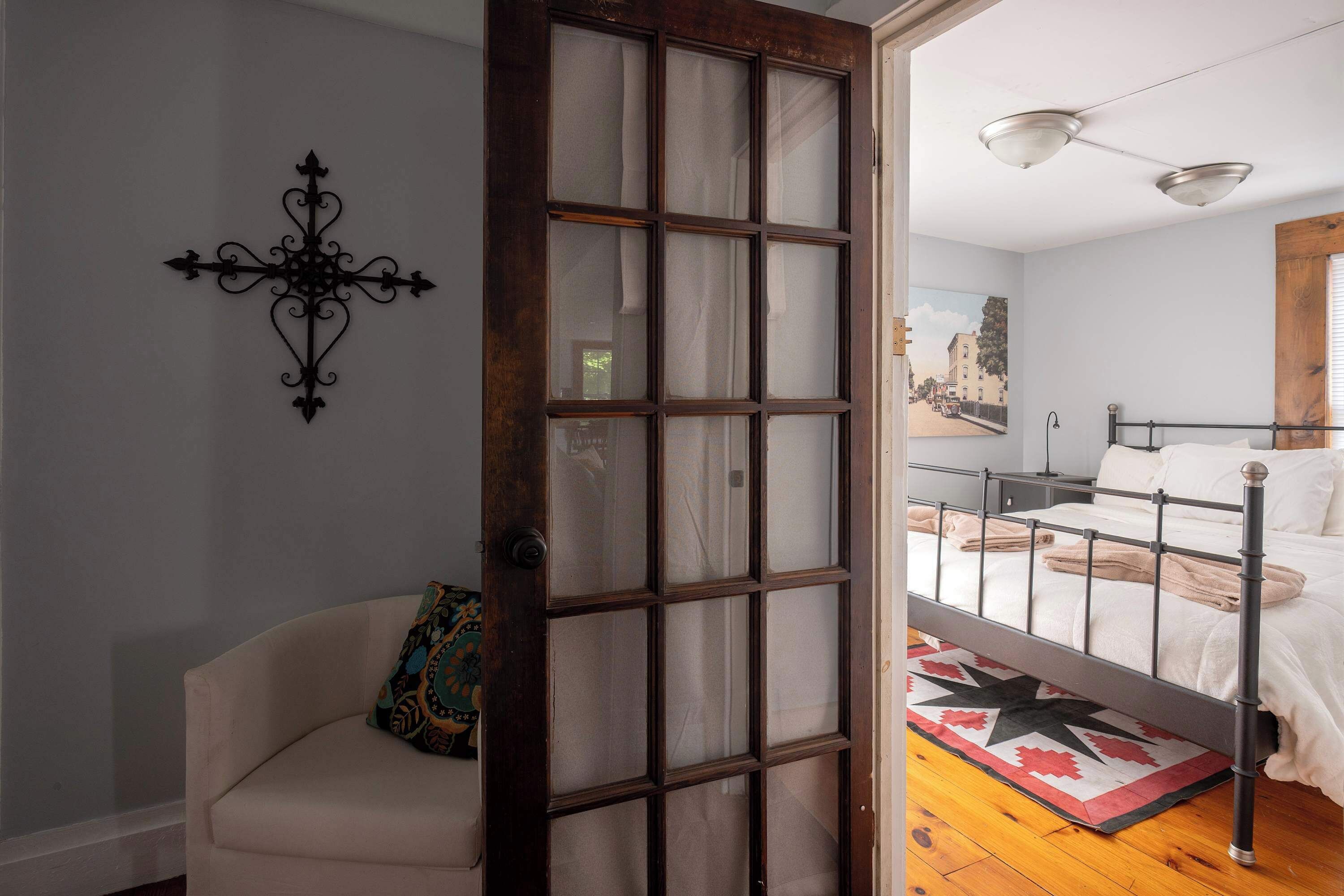 A bedroom with a bed, a nightstand, a window with a view of a street, and a door leading to another room.