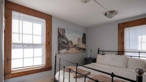 A bedroom with a bed, a nightstand, a wall-mounted lamp, and a painting. - Historic Main St. Rosendale Apt (Rosendale)