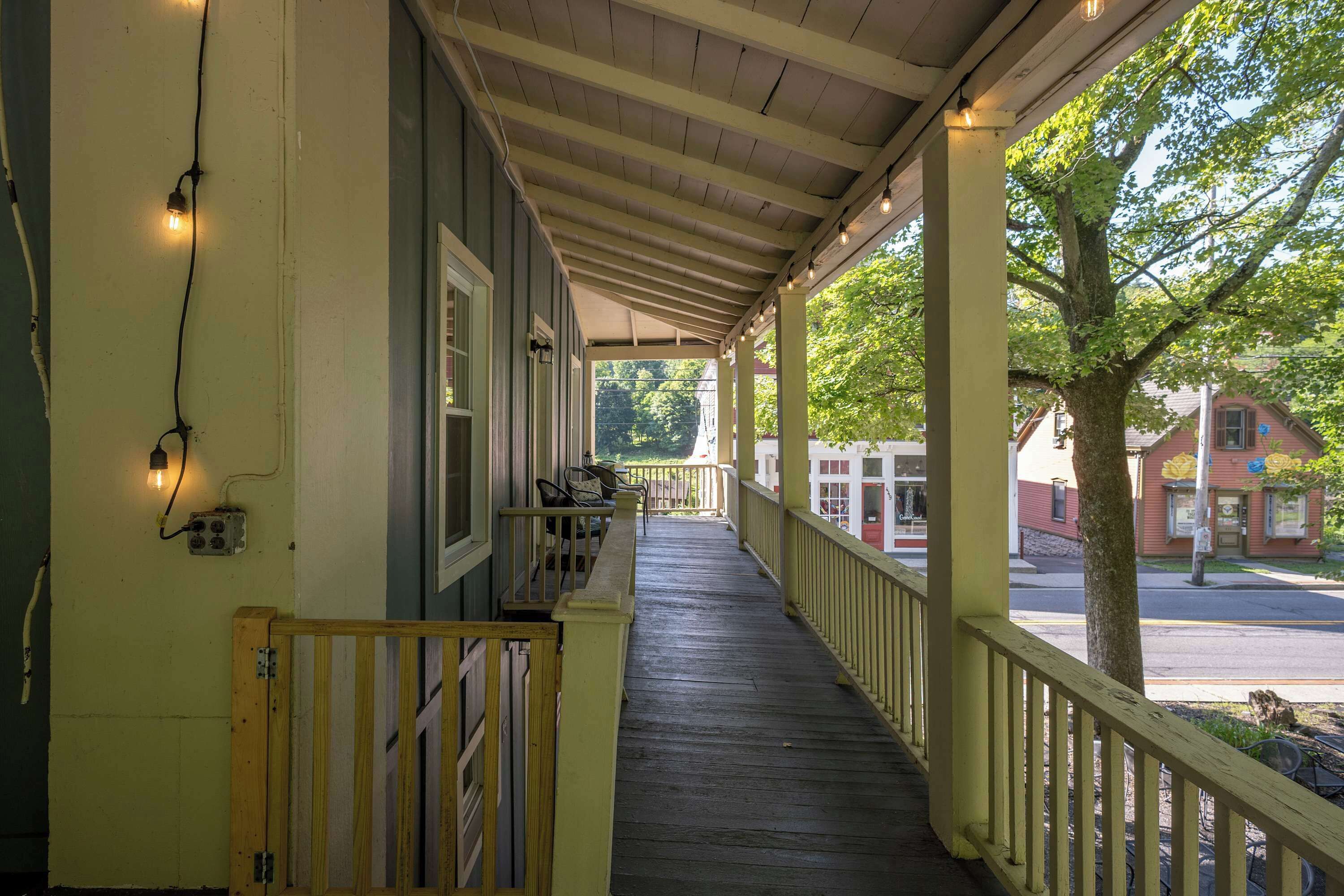 A covered porch with a wooden railing, a bench, and a view of the street and buildings in the background.