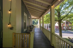 A covered porch with a wooden railing, a bench, and a view of the street and buildings in the background. - Historic Main St. Rosendale Apt (Rosendale)