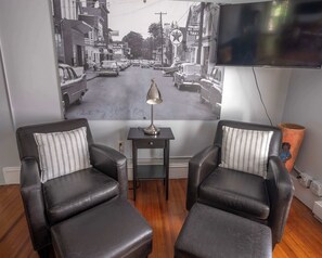A room with two leather armchairs, a small table with a lamp, and a large wall mural of a street scene.