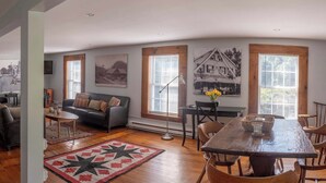 A spacious living area with a sofa, a dining table, and a coffee table. There are large windows with blinds, a fireplace, and a wall-mounted TV. - Historic Main St. Rosendale Apt (Rosendale)