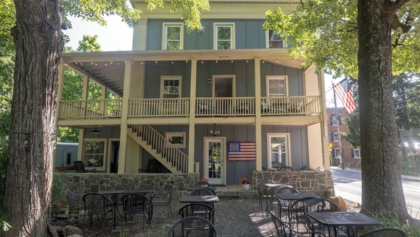 A two-story building with a balcony, outdoor seating, and an American flag. - Historic Main St. Rosendale Apt (Rosendale)