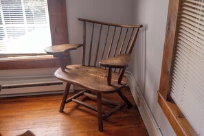 A corner room with a wooden rocking chair, a window with blinds, and a radiator.