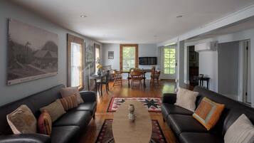 A spacious living room with a large painting, a dining area with wooden furniture, and a kitchen visible through an open door.